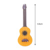 A yellow miniature acoustic guitar with a long neck and tuning peg, shown next to a vertical measurement line.