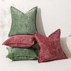 A grouping of four soft chenille throw pillows in shades of moss green and dusty rose on a white surface.