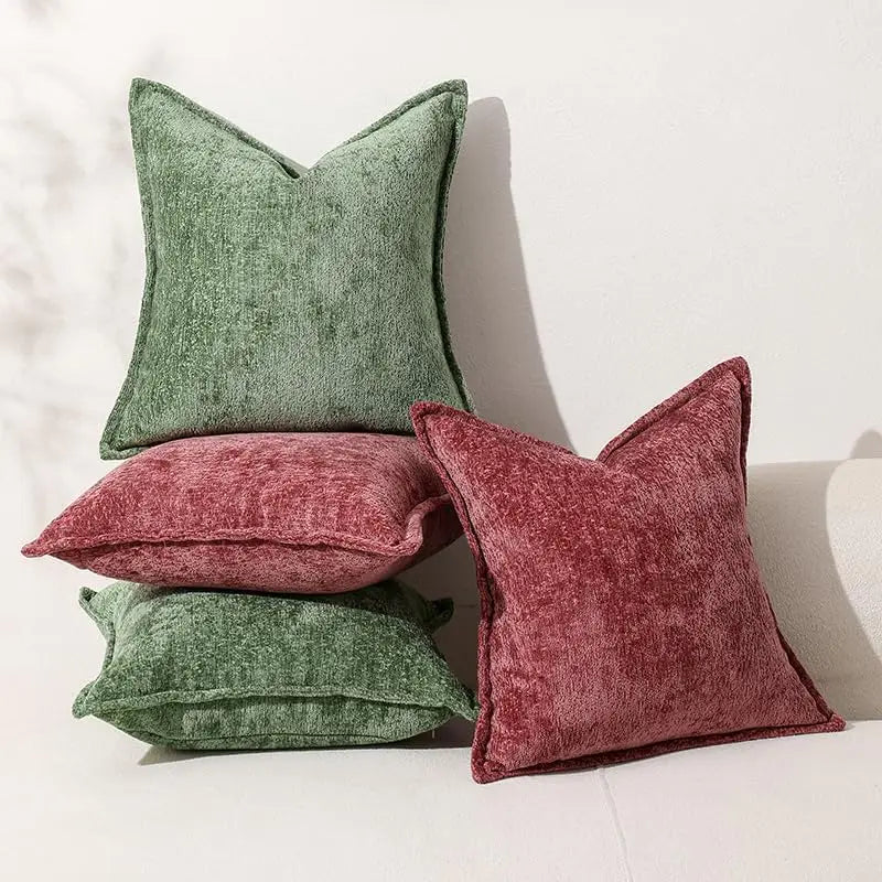 A grouping of four soft chenille throw pillows in shades of moss green and dusty rose on a white surface.