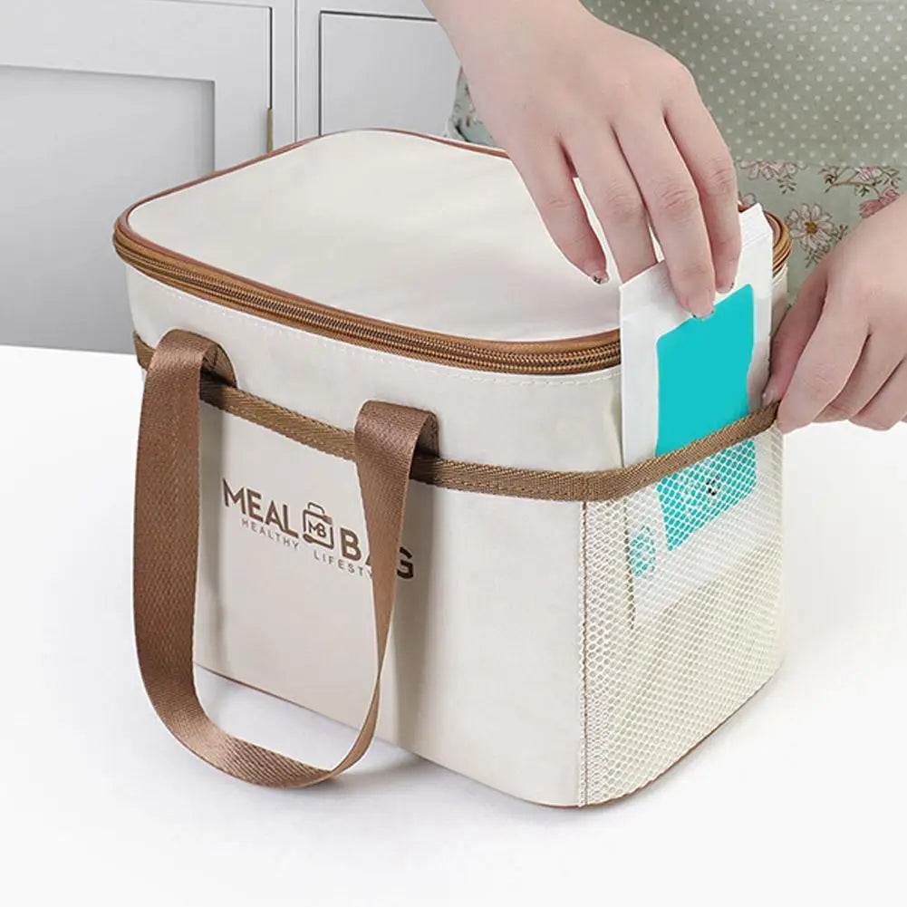 A beige insulated lunch bag with a brown strap and a teal lining is being held by a hand.