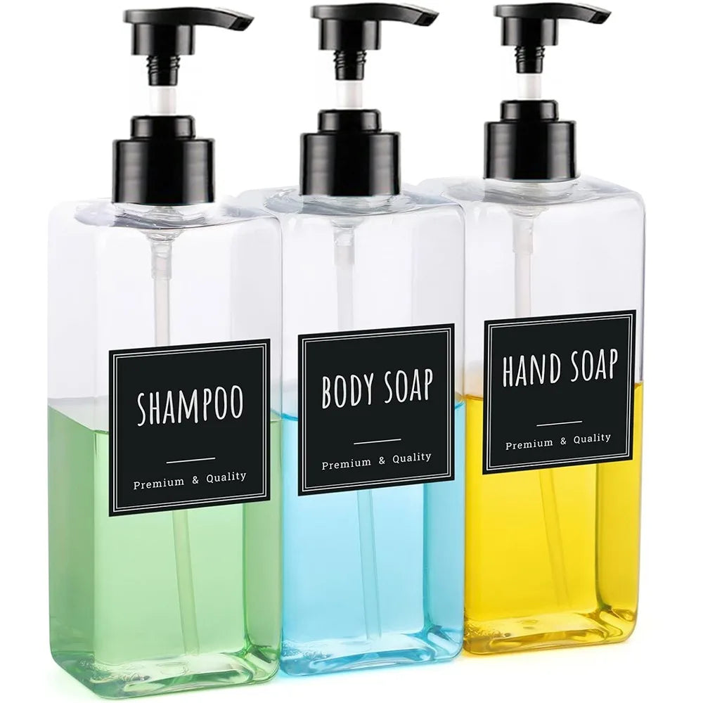 A three-pack of clear glass refillable soap dispenser bottles with black pump tops and labels for shampoo, body soap, and han