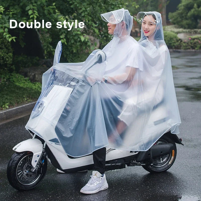 A woman wearing a transparent waterproof motorcycle rain poncho with hood rides a white scooter on a wet road.