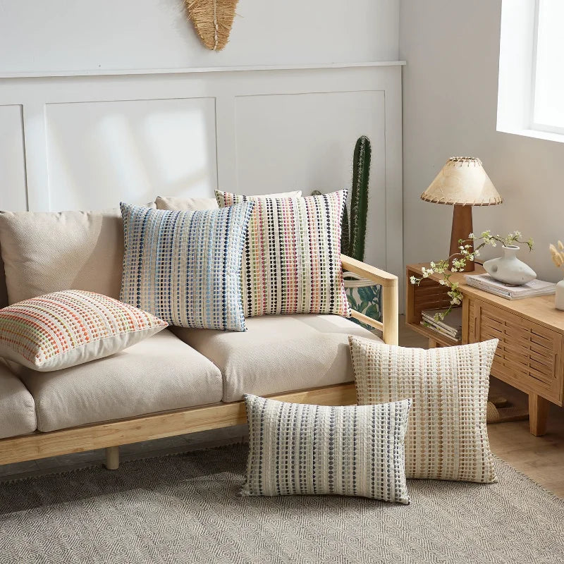A set of two bohemian linen pillow covers in muted pastel and earthy tones displayed on a light-colored sofa.