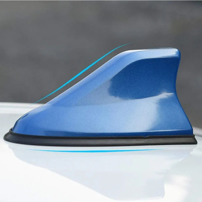 Blue aerodynamic shark fin car antenna with signal amplifier mounted on a white surface.