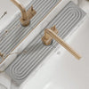 A brass faucet mat with a wavy design is installed on a white countertop next to a sink.
