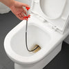 A hand is using a red drain unclogging tool with an ergonomic handle to clear a toilet drain.
