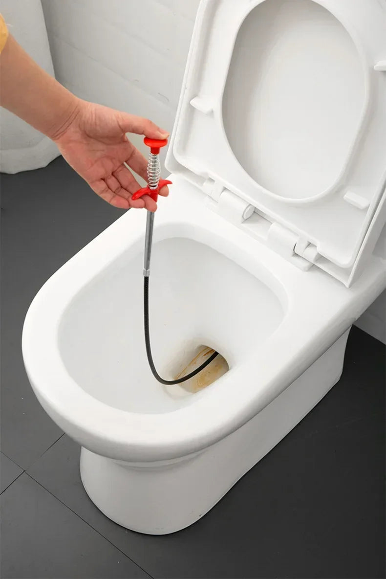 A hand is using a red drain unclogging tool with an ergonomic handle to clear a toilet drain.