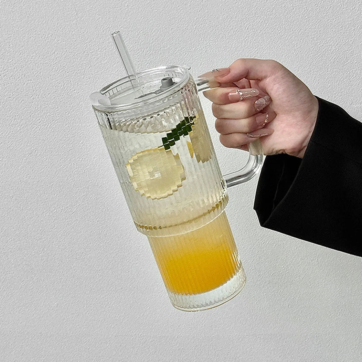 A hand holds a ribbed glass tumbler filled with yellow-orange liquid and ice, garnished with green leaves.