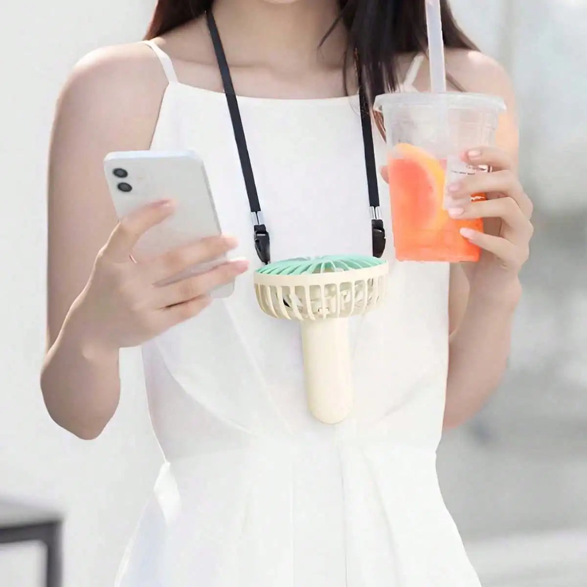 Una mujer sostiene una blusa blanca y una taza transparente con una bebida naranja mientras mira un smartphone.