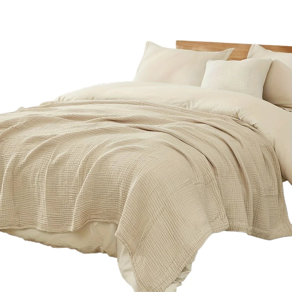 Beige, große 6-lagige Baumwollgaze-Decke über einem Bett mit weißen Kissen.