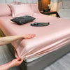 Un juego de sábanas ajustadas de algodón rosa de lujo se muestra en una cama con almohadas y un artículo decorativo gris oscu