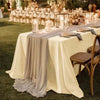 A long table set with a cream satin tablecloth and gray draping, ready for a wedding or formal dining event.
