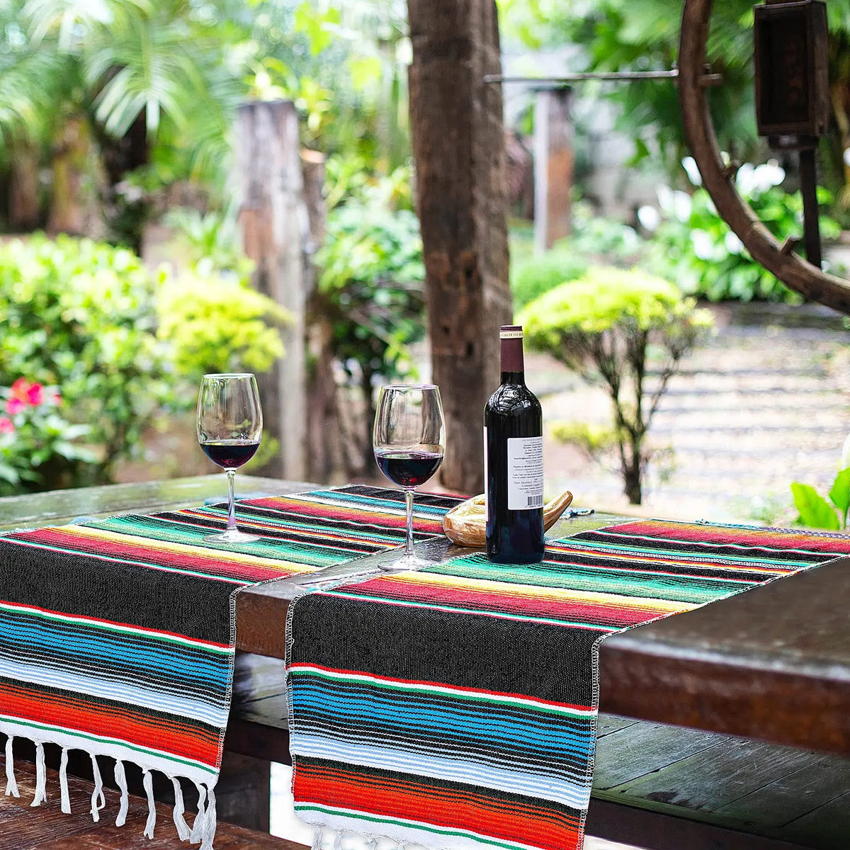 A vibrant Mexican serape table runner with colorful stripes and tassels displayed on a wooden table.