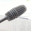 A silicone bottle brush with a long handle is shown cleaning the inside of a glass container.