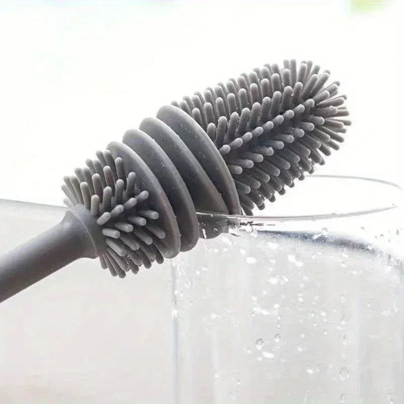 A silicone bottle brush with a long handle is shown cleaning the inside of a glass container.