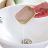 A hand is dripping liquid from a compact travel soap holder into a white sink basin.