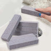 A hand is holding a gray pumice stone cleaning block used for scrubbing toilets, tiles, and sinks.