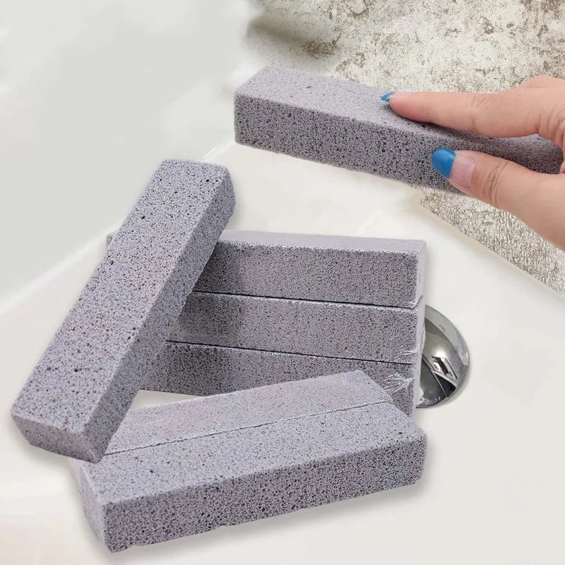 A hand is holding a gray pumice stone cleaning block used for scrubbing toilets, tiles, and sinks.
