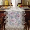 A white lace table runner with a floral pattern is displayed on a dark wooden table.