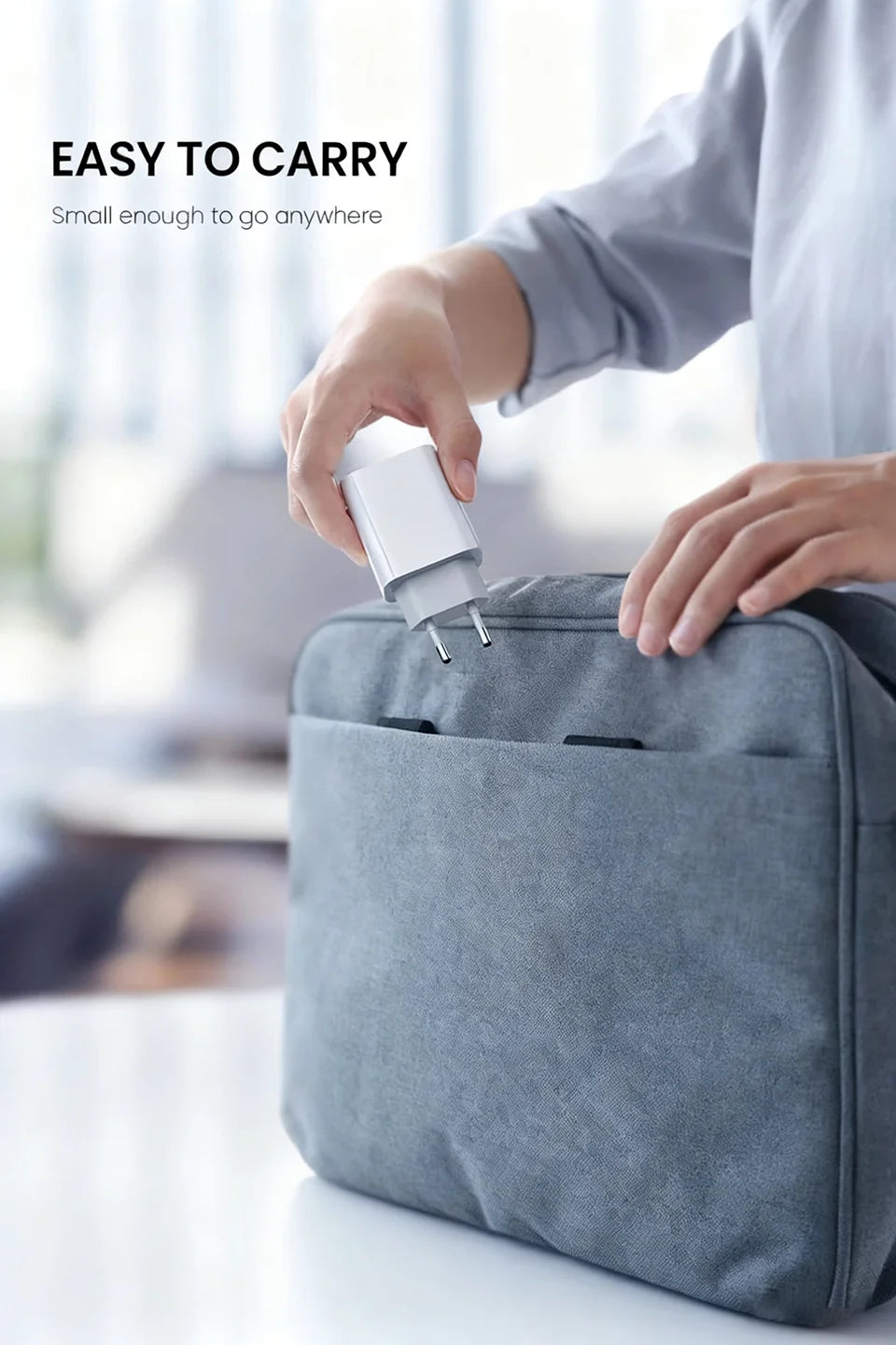 Eine Hand steckt ein weißes Ladekabel in eine graue Tasche, was die einfache Tragbarkeit demonstriert.