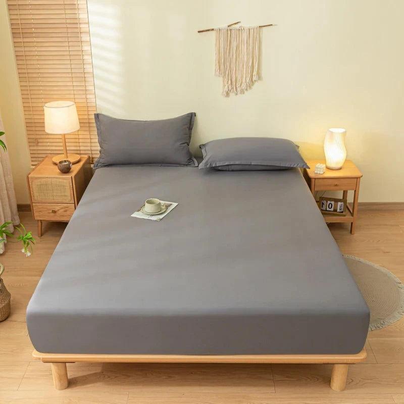 A gray fitted bed sheet set with pillowcases is displayed on a wooden bed frame in a bright bedroom.