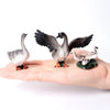 A hand holds several realistic animal figurines, including a large goose and smaller birds, for a farm and wildlife collectio