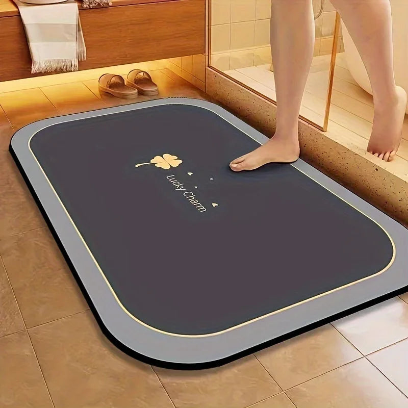 A dark gray diatomite bath mat with a gold border is placed on a tiled floor next to a wooden cabinet.