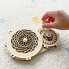 A hand is assembling a wooden puzzle featuring gears and a decorative wheel for a toddler learning busy board kit.