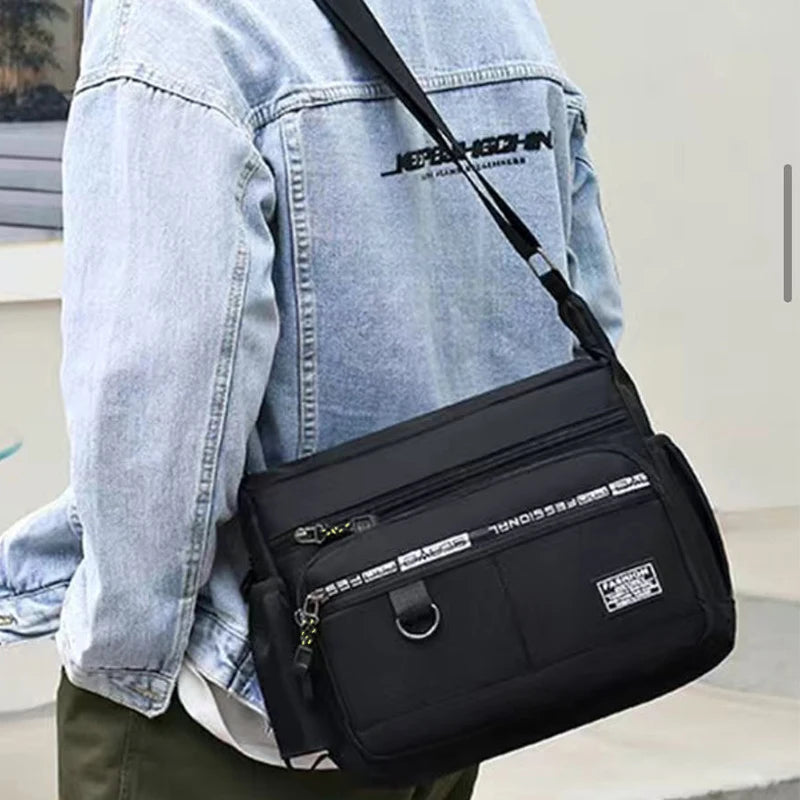 Eine Person trägt eine Jeansjacke und hält eine schwarze, leichte Umhängetasche mit organisiertem Stauraum.