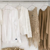 A collection of ten natural fiber and wire clothes hangers displaying various light-colored and beige garments.