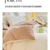 A beige velvet blanket is draped over a white duvet on a bed, with pillows and bedding visible.