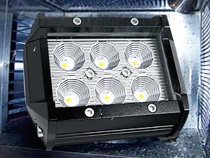 A black LED flood light pod with four circular light elements is mounted inside a vehicle's light bar housing.
