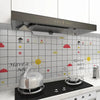 A stainless steel kettle sits on a stovetop in front of a white kitchen splashback decorated with colorful stickers.