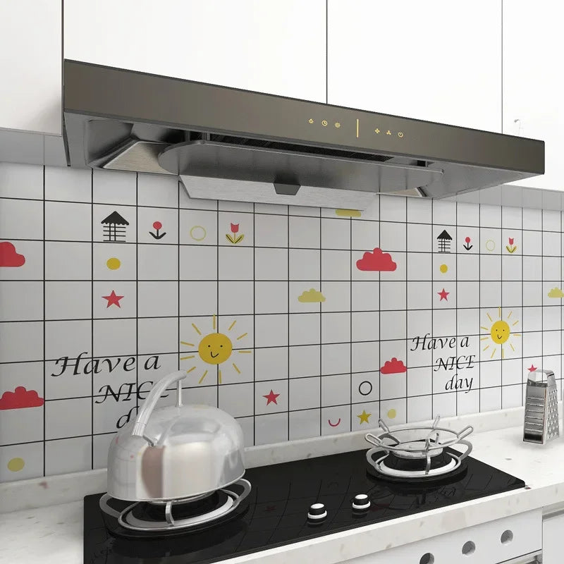 A stainless steel kettle sits on a stovetop in front of a white kitchen splashback decorated with colorful stickers.