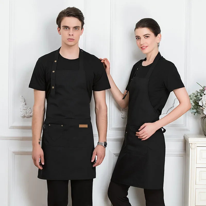 Two models wearing black adjustable cotton aprons standing in front of white paneled doors.