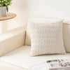 A white knitted pillowcase with a textured pattern resting on a light-colored sofa.