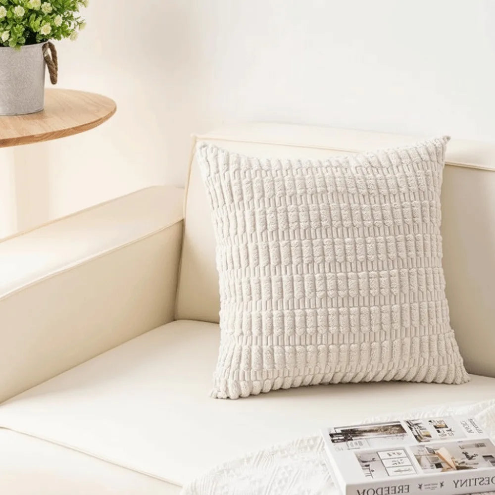 A white knitted pillowcase with a textured pattern resting on a light-colored sofa.