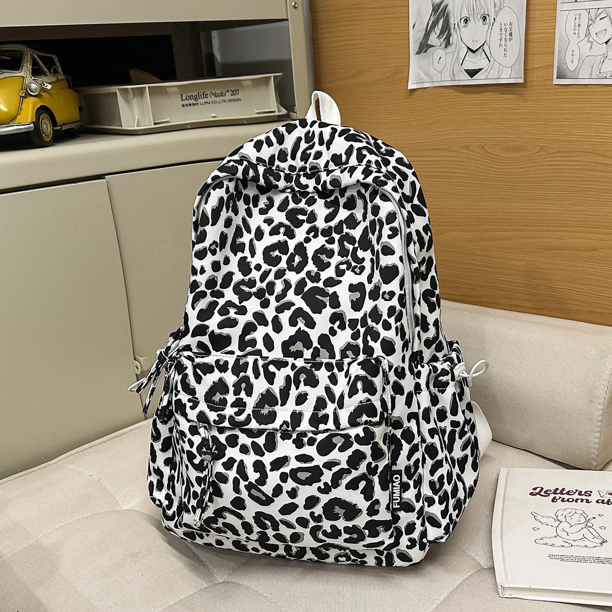 A white and black leopard print nylon backpack with multiple pockets resting on a light-colored surface.