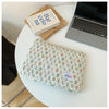 A floral printed laptop sleeve with a zipper closure resting on a white table next to a book and a silver laptop.