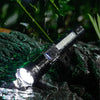 A black LED flashlight with a bright beam is shown shining on wet rocks in a dark, natural setting.
