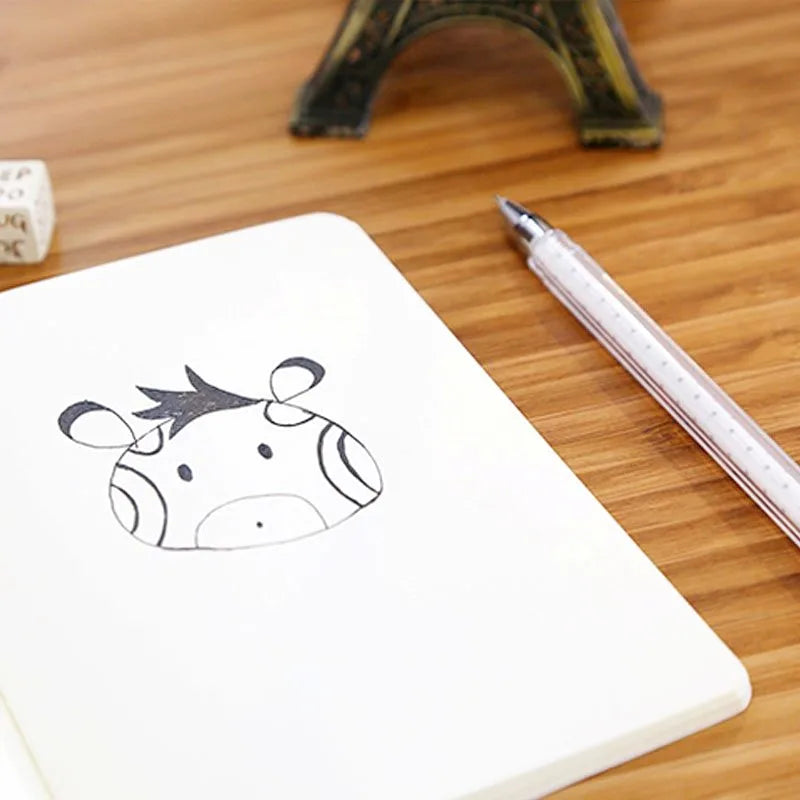A white A6 kraft paper blank notebook with a simple black line drawing of a horned animal on the cover, next to a silver pen.