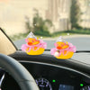 A pink and yellow rubber duck car decoration with a crown, sunglasses, and pearl necklace placed on a car dashboard.