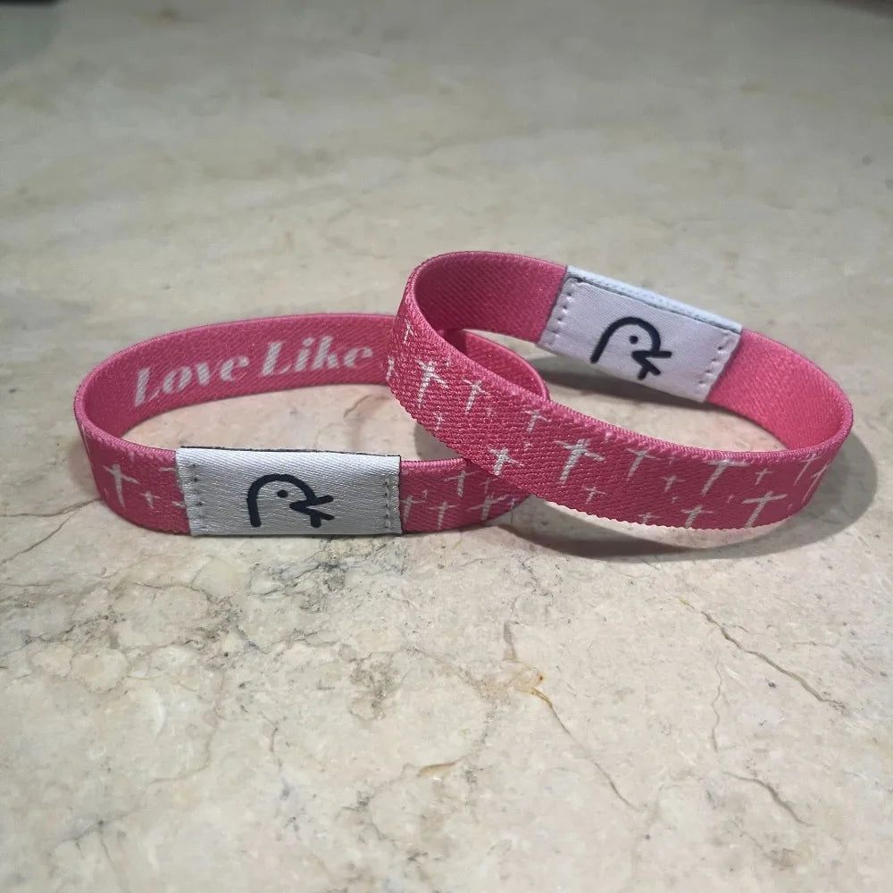 A pink NFC Bible verse bracelet with white text and a cross design on the band.