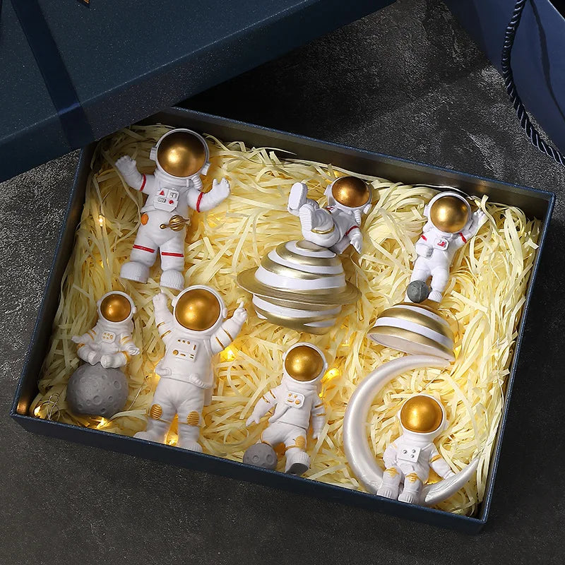 A collection of handcrafted astronaut figurine resin spacemen in white suits and gold helmets displayed in a dark box.