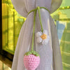 Handmade crochet strawberry pendant with a white flower detail hanging from sheer lilac fabric.