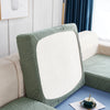 A close-up of a sage green stretch jacquard sofa cover with an anti-slip backing and white cushion on a light-colored sofa.