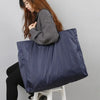 A person is holding a navy blue reusable large-capacity grocery tote with a zipper on a white stool.