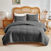 A gray quilted queen bedspread set with matching pillow shams displayed on a bed.