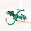 A green enamel dragon brooch with rhinestone accents is displayed on a white surface next to a white candle.