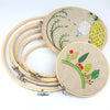 A set of bamboo embroidery hoops with adjustable screws and embroidery thread on a beige fabric.